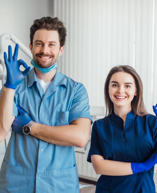 Photo of smiling dentist standing with arms crossed with her colleague, showing okay sign.